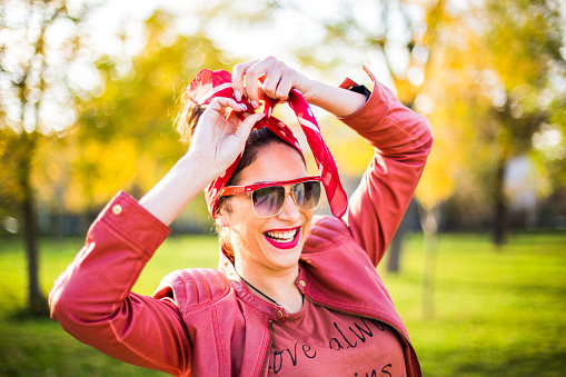 Portrait of a smiling young woman fixing headband in the city park on a beautiful sunny autumn day