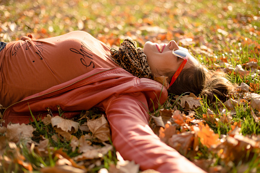 Portrait of a beautiful young woman lying down in yellow leaves in the city park on a sunny autumn day