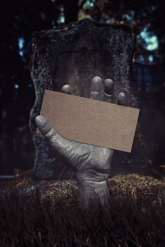Zombie hand rising out of the ground holding cardboard. Halloween theme. Add your text.