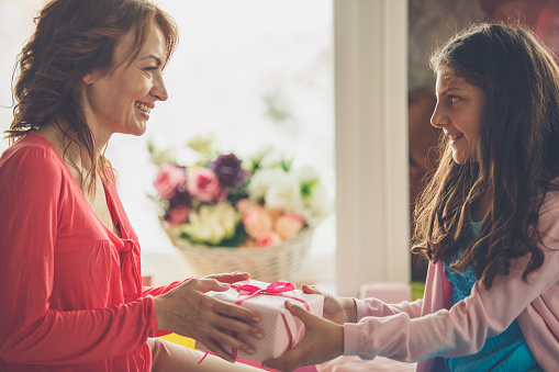 Cheerful young girl giving her mother a nicely wrapped pink present for Mother's day.