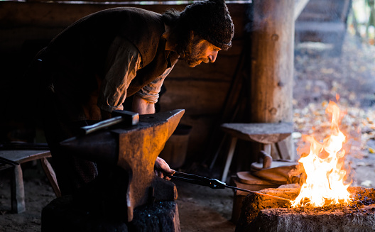 An individual viking male blacksmith working on his anvil in a viking settlement village setting