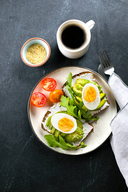 istock Avocado toasts with cottage cheese, eggs, arugula on darl table. Healthy breakfast, snack. Top view 1280477775