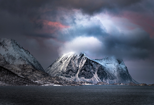 Beautiful view on Norwegian sea and snowcapped mountain range during winter blue hour in Steinfjord, Norway.