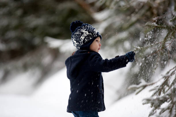 netter junge spielt mit teddybär im schnee, winterzeit. kleines kleinkind spielt mit spielzeug am verschneiten tag - little boys sled clothing slide stock-fotos und bilder