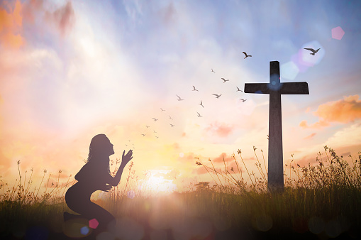 Silhouette woman hand rising for worship God over cross on sunset background