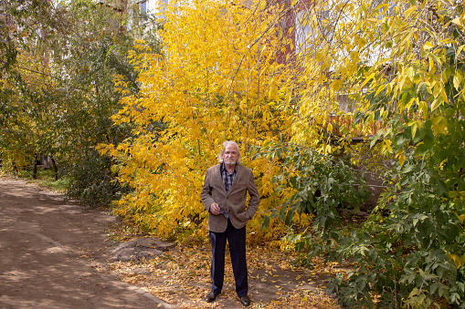 elegantly dressed grandfather walks through the autumn forest among bright yellow trees