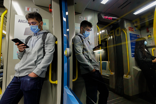 October 15, 2020: Young man wearing a face mask traveling on the Porto subway metro looking at his smartphone during the covid-19 pandemic