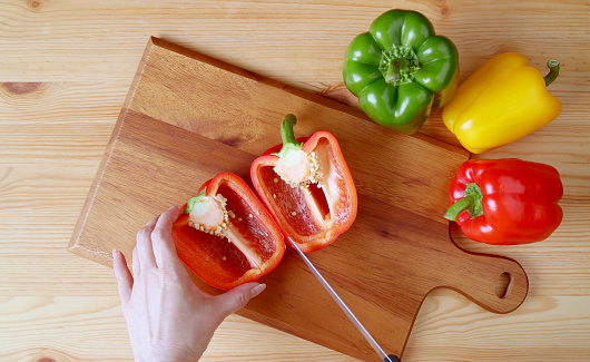 Top View of Hand Cutting Red Bell Pepper on a Wooden Cutting Board with Three-color Bell Peppers Scattered Around