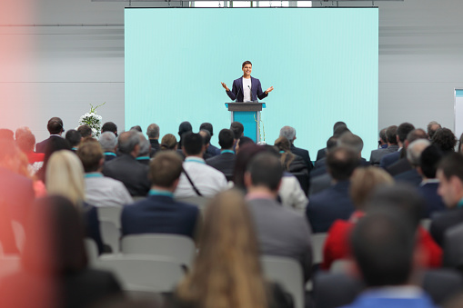 Man speaking on a pedestal on a conference in front of an audience isolated on white background