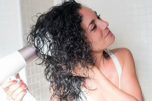 Young woman in profile smiling curling her hair with a hairdryer with a special nozzle for curling her hair. dryer with diffuser. care and beauty concept.