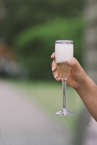 a prosecco glass in a woman's hand outdoors with green background