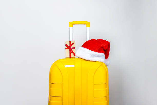 istock On a yellow plastic suitcase is a gift and wearing a red Santa Claus hat on a light background 1280494114