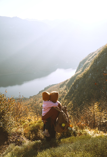 Mother and daughter together outdoors. Young woman with camping backpack and little child girl relaxing on top of mountain. Beautiful happy family on a hike. Adventure travel with kids in nature.