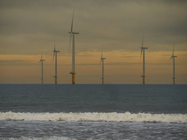 Redcar Image covering the structural economic changes in the North-East of England. Image shows the burgeoning new industry of sustainable energy generation, consisting of the near-shore wind farm at Redcar Beach, showing waves breaking in the foreground and the wind farm on the horizon against a deeply coloured, scenic cloudy sky. teesside northeast england stock pictures, royalty-free photos & images