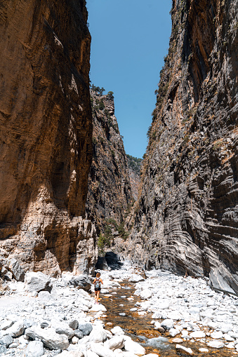 Dry river bed in Samaria Gorge and woman tourist walking on the rocks. Vertical photo of a tourist attraction on Crete, Greece.