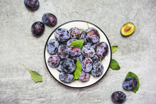 A lot of fresh sweet plums in a plate with leaves, top view with space for text. Healthy fruits.