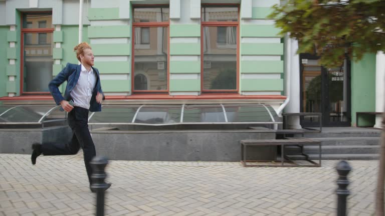 Young man in office suit with smartphone runs along street