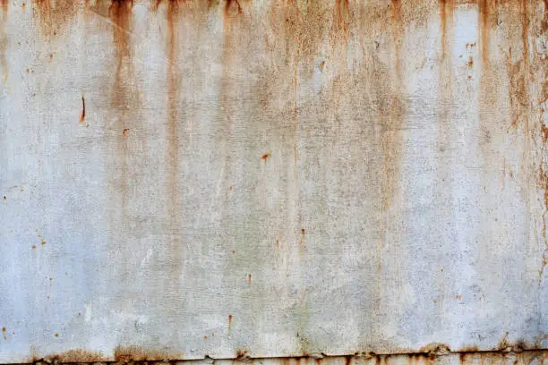 Photo of The old metal wall is painted with white paint. Centers of corrosion and rust streaks are visible. Background. Texture.