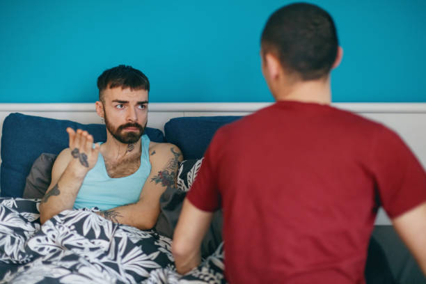 Looking at his boyfriend and gesturing, having an argument in bed Young gay man in bed looking at his boyfriend and explaining, using hand gesture, LGBT break up sad gay stock pictures, royalty-free photos & images