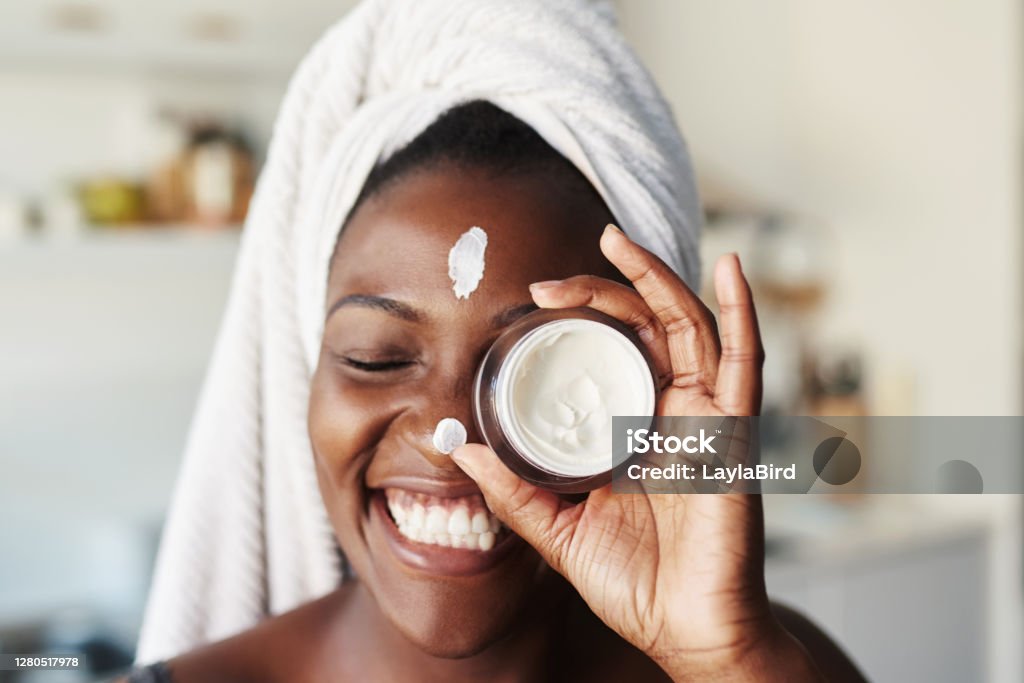 I love taking care of my skin Shot of a beautiful young woman holding up a face cream product Skin Care Stock Photo