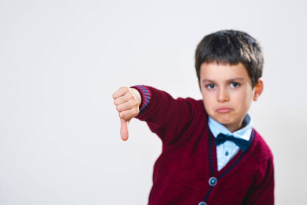 istock Schoolboy in a sweater shows a thumb down with a negative facial expression. Focus on the hand. Conceptual. Copy space. 1280518582