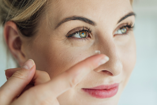 A side view, close-up shot of a beautiful blonde woman putting in a contact lens.