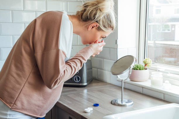 Morning Routine A side view shot of a beautiful blonde woman standing in her kitchen by the window. She is bending over and looking into the mirror whilst putting in her contact lenses. inserting stock pictures, royalty-free photos & images