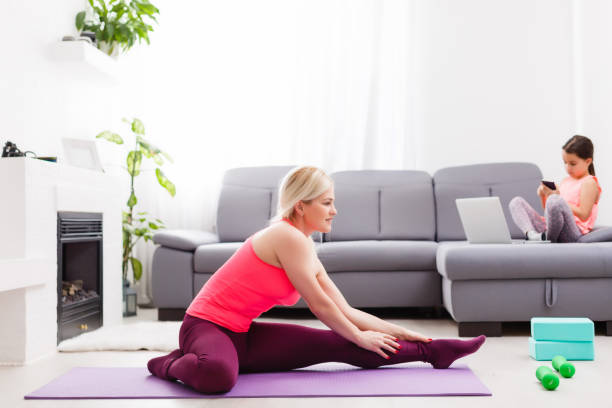 女性は、彼女のリビングルームで自己隔離中にラップトップでオンラインヨガをしています, 機器のトレーニングなし, 初心者のための瞑想のヒント.子供たちとの家族の時間は、家にいなさ� - yoga business women living room ストックフォトと画像