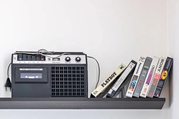 Photo of Vintage cassette recorder and videotapes on the shelf.