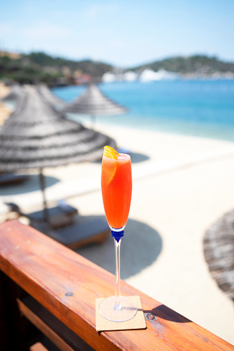 small orange cocktail paper umbrella on the beach sand with the sunlight in the evening, copy space