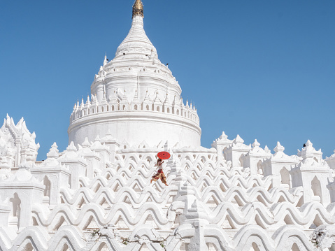 A Burmese Buddhist novice monk walking around the white stupa in sunny day.