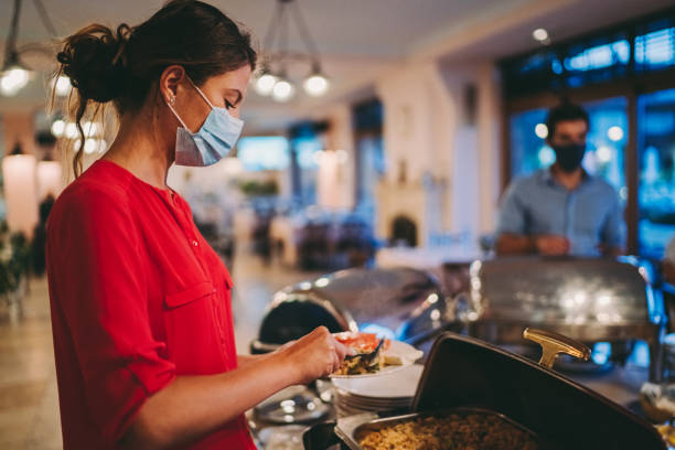 Covid tourism and hotel reopening Hotel guests with protective face masks are keeping social distance in the hotel restaurant buffet hotel people women stock pictures, royalty-free photos & images