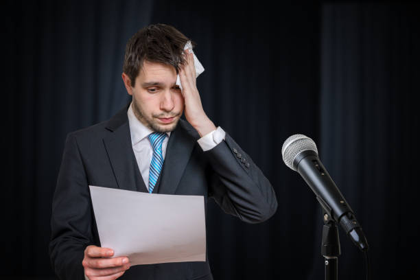 Sweating nervous speaker is afraid of public speech. Microphone in front.