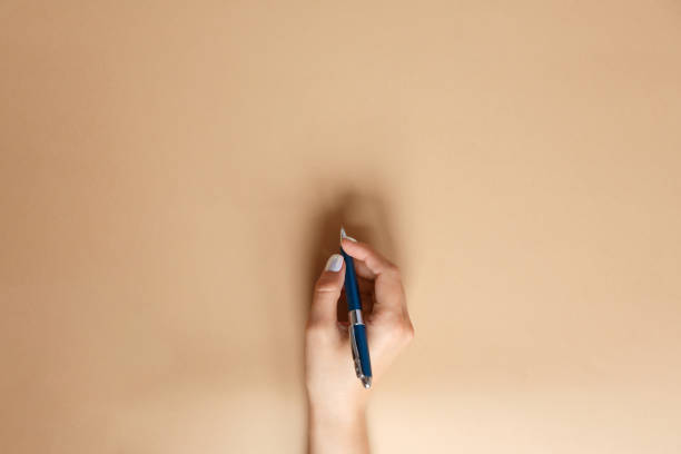 Gesture and sign, hand holds a pen on a brown background Gesture and sign, female hand holding a metal blue pen and writing on a brown background, flat lay copywriter photos stock pictures, royalty-free photos & images