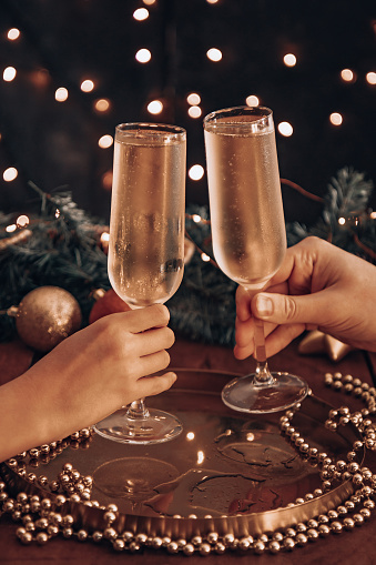 Hands hold glasses of champagne and check out among the Christmas lights. High quality photo