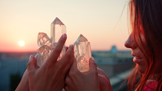 Two sisters holding healing crystals on of palm of their hands. Cityscape at sunset in background
