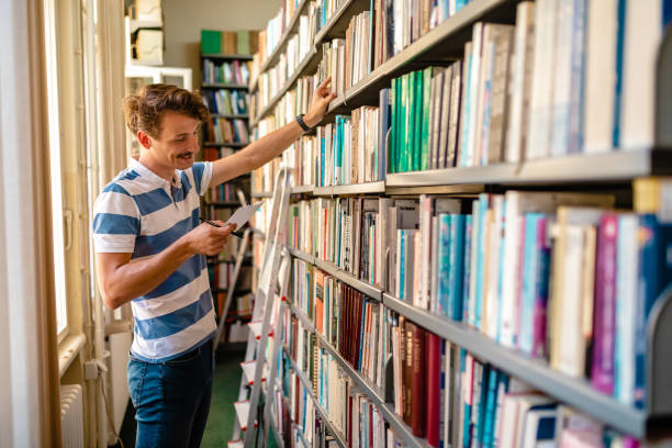 istock Diligent librarian looking for a book the user need, between shelves at the library 1280573539