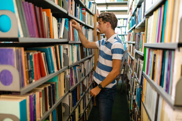 istock Student looking for a literature between bookshelves at University library 1280574039