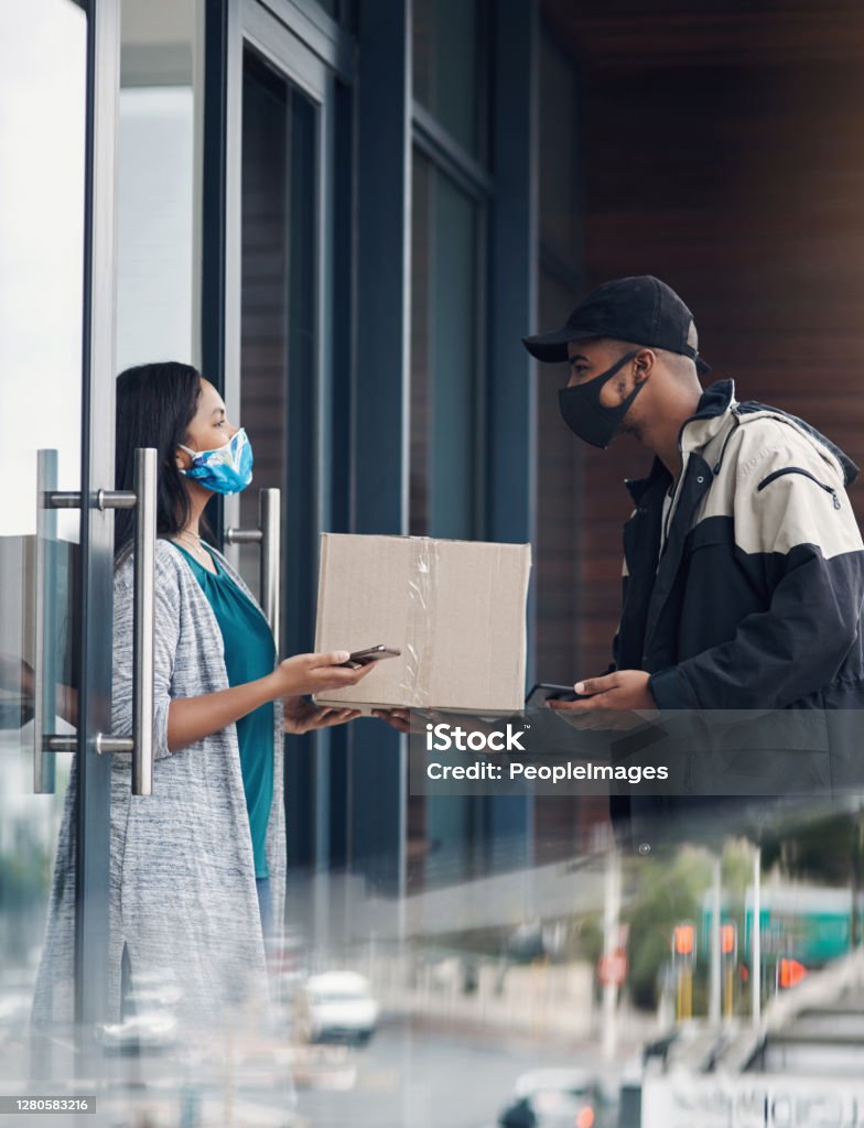We care for your safety so lets keep the distance Shot of a masked young woman receiving a delivery at home Delivering Stock Photo