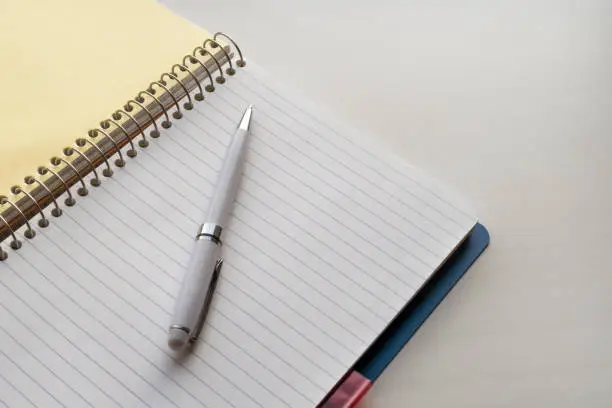 White pen and open spiral notebook on white table. Background image with copy space for text.