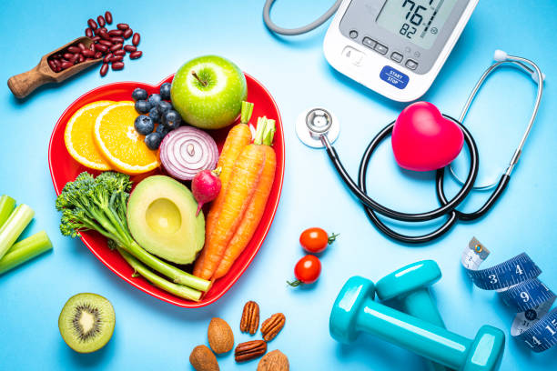 Healthy eating, exercising, weight and blood pressure control Healthy lifestyle concepts: red heart shape plate with fresh organic fruits and vegetables shot on blue background. A digital blood pressure monitor, doctor stethoscope, dumbbells and tape measure are beside the plate  This type of foods are rich in antioxidants and flavonoids that prevents heart diseases, lower cholesterol and help to keep a well balanced diet. High resolution 42Mp studio digital capture taken with SONY A7rII and Zeiss Batis 40mm F2.0 CF lens wellness concept stock pictures, royalty-free photos & images