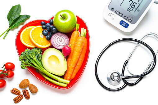 Healthy lifestyle concepts: red heart shape plate with fresh organic fruits and vegetables shot on white background. A digital blood pressure monitor and  doctor stethoscope are beside the plate. This type of foods are rich in antioxidants and flavonoids that prevents heart diseases, lower cholesterol and help to keep a well balanced diet. High resolution 42Mp studio digital capture taken with SONY A7rII and Zeiss Batis 40mm F2.0 CF lens