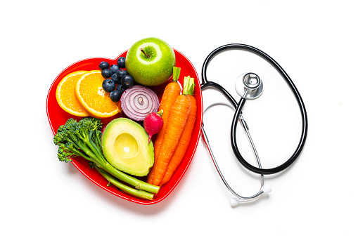 Healthy lifestyle concepts: red heart shape plate with fresh organic fruits and vegetables shot from on white background. A doctor stethoscope is beside the plate. This type of foods are rich in antioxidants and flavonoids that prevents heart diseases, lower cholesterol and help to keep a well balanced diet. High resolution 42Mp studio digital capture taken with SONY A7rII and Zeiss Batis 40mm F2.0 CF lens
