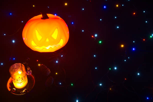 Beautiful and cozy Halloween theme background with glowing pumpkin, burning candle, scary spider, candies and color lights on black backdrop with copy space stock photo