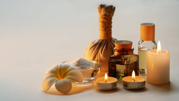 Beautiful spa composition with candles, frangipani flower, oil flasks, bowl with salt and herbal ball. Copy space. stock photo