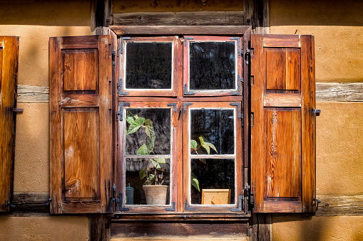 Window with brown frame on a blue house and a window box full of summer flowers