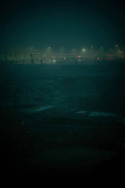 Futuristic wide scene of a post-apocalyptic wasteland with silhouettes of people in the distance waiting for transportation illuminated by street lights in the green smog that surrounds them