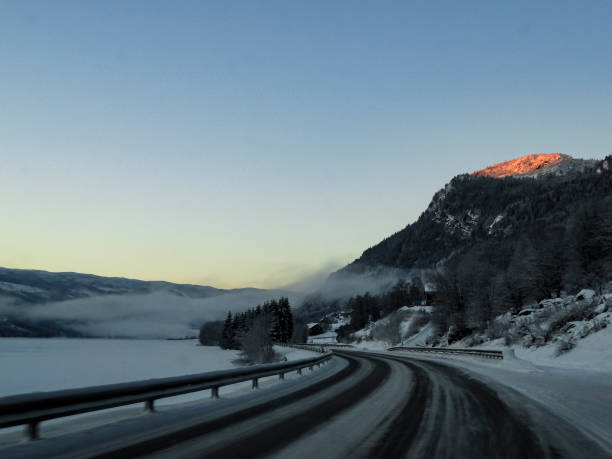 Driving at sunrise through mountains and forests in Norway. Sunshine on a mountain top.