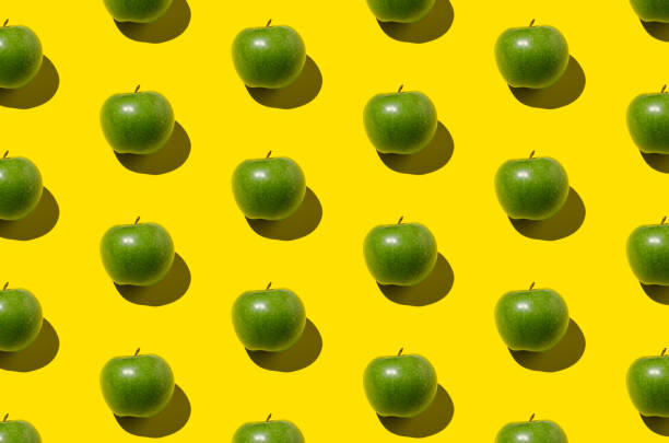 istock Green apple pattern on a yellow background. Hard shadows, overhead. 1280623131