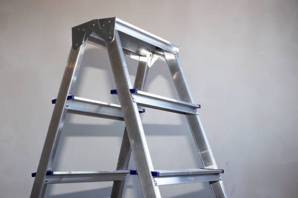 una escalera de hierro se encuentra en una habitación con paredes de yeso gris, una copia del espacio - escaleras de aluminio fotografías e imágenes de stock